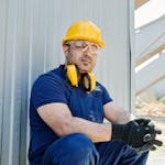 A male construction worker wearing safety gear sits at a construction site, showcasing standard industry protection.